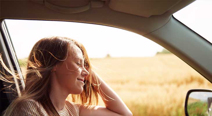 Photo of a woman in a car with the window down on a sunny day