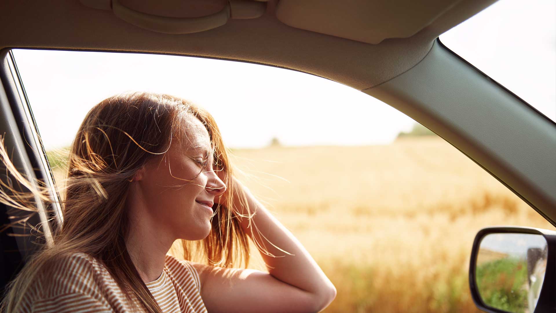 Photo of a woman in a car with the window down on a sunny day