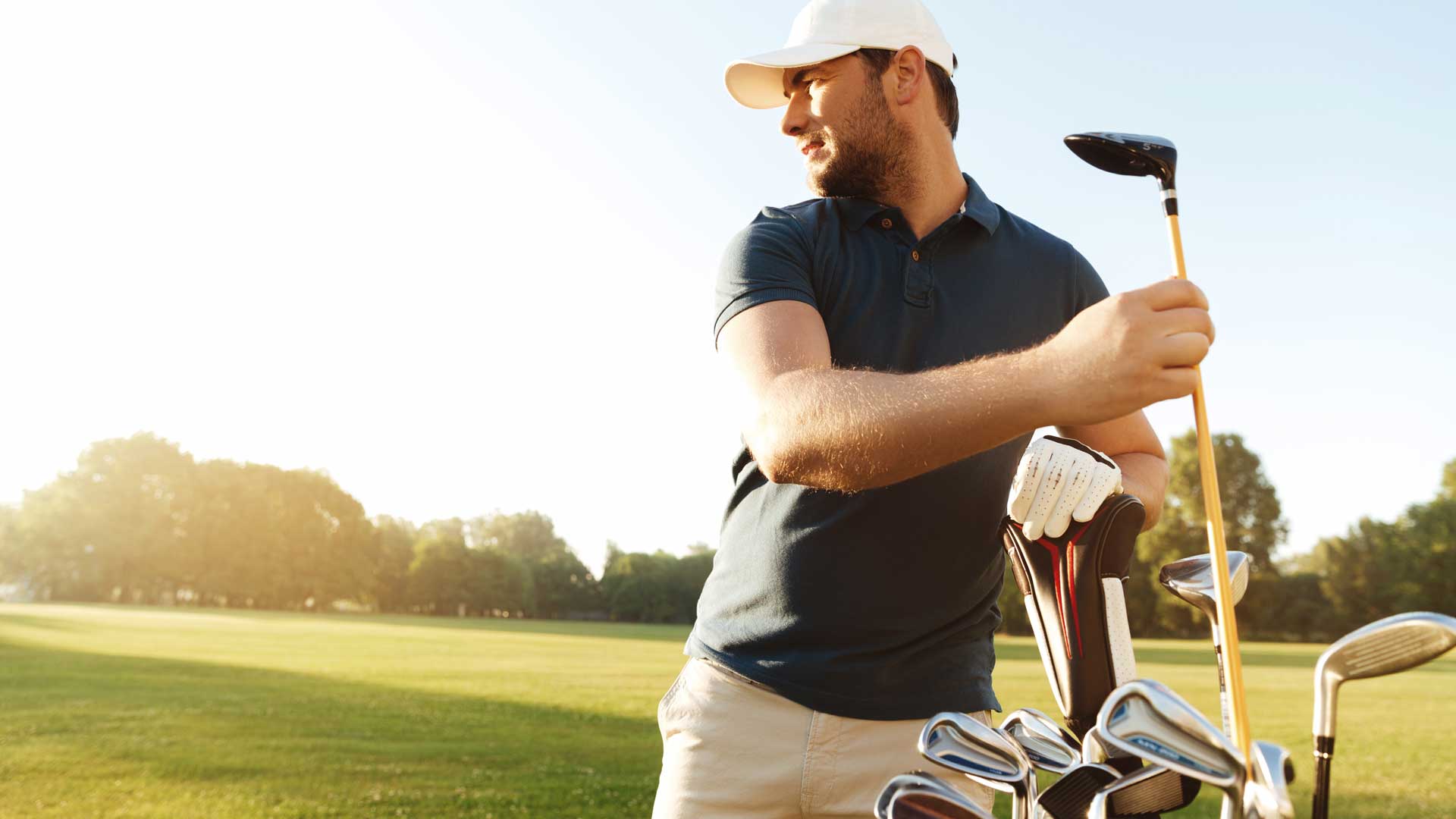 Photo of a man taking a golf club out of a bag on a sunny day